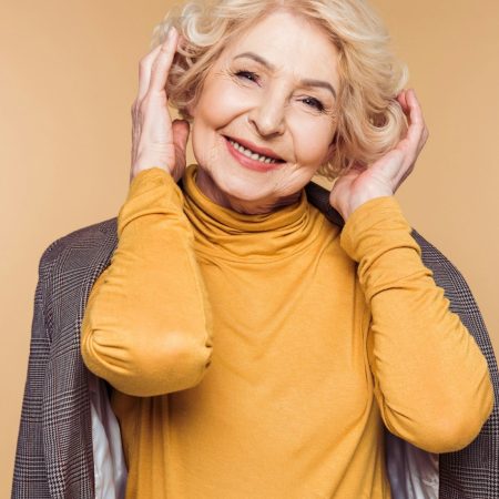senior woman with jacket on shoulders adjusting haircut isolated on beige background